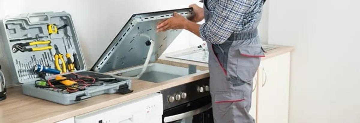 Cooktop repair technician lifting a built-in stovetop for service in Sioux Falls, SD