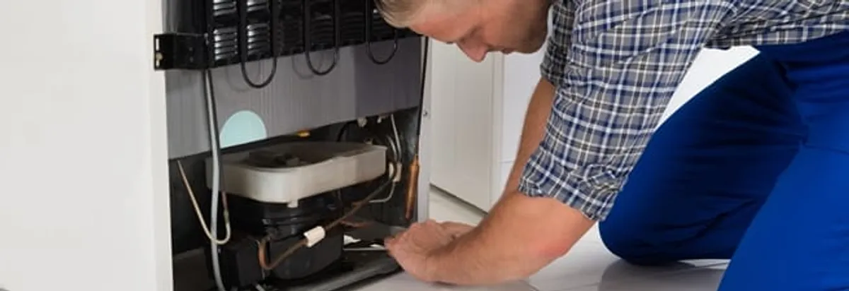 Refrigerator repair technician servicing the compressor and condenser area in Sioux Falls, SD